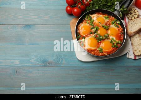 Delicious Shakshuka in frying pan served on light blue wooden table, flat lay. Space for text Stock Photo