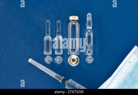 Blank vaccine vial, medical mask and syringe on blue background with copy space, top view. Stock Photo