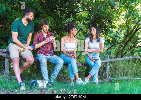 Group of diverse friends using smartphones and laughing together in a lush park. Stock Photo