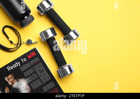 Metal dumbbells, whistle, magazine and plastic bottle on yellow background, flat lay. Space for text Stock Photo