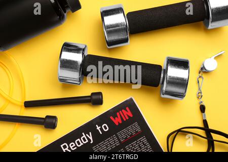 Metal dumbbells, whistle, magazine and skipping rope on yellow background, flat lay Stock Photo