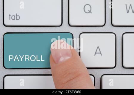 Woman pressing turquoise button with word Payroll on keyboard, top view Stock Photo
