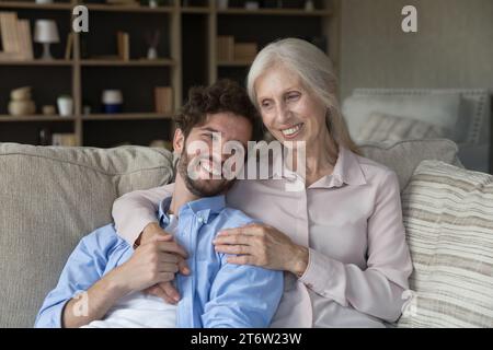 Mature woman hugging adult son resting on sofa at home Stock Photo