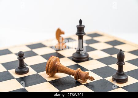 Chess game with black and white pieces on the chessboard. White king defeated, black pawn, bishop and king standing. High quality photo Stock Photo
