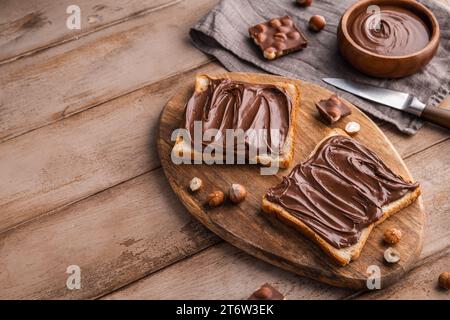 Board of bread with chocolate paste and hazelnuts on wooden background. Popular desser food. Top view. Stock Photo
