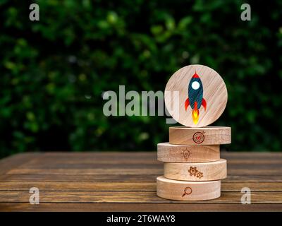 Rocket symbol on round wood on top of business strategy icons on wooden block stack on table on green leaves background with copy space. Small busines Stock Photo