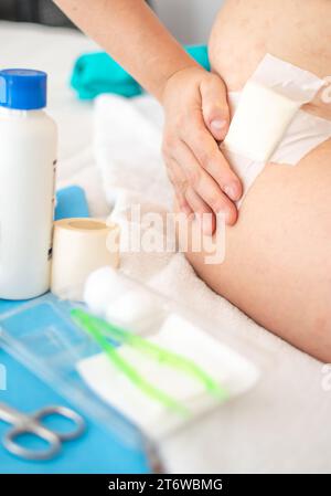 Close up view of hand touching wound with gauze on hip and Aid Kit utensils Stock Photo