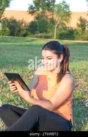 Young Caucasian woman smiling and happy using tablet sitting in park Stock Photo