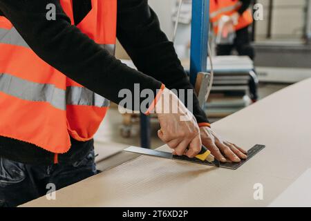 Worker cutting cardboard with utility knife and ruler, closeup Stock Photo