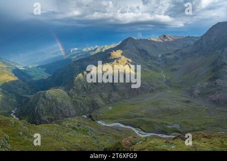 After the rain storm, mountains are illuminated by filtering sunlight and a rainbow appears. Beautiful sky before sunset in the high alpine country. Stock Photo