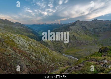 After the rain storm, fluffy clouds form in the sky and a rainbow appears. Beautiful sky at sunset in the high alpine country. Stock Photo