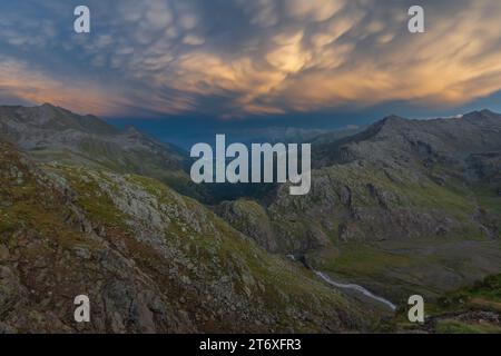 Vivid sky after a thunderstorm in the mountains, with puffy clouds painted orange by the last sunrays. Mountain ridge and stream in the Italian Alps. Stock Photo