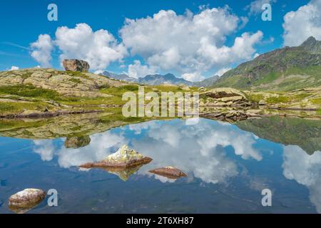 Sky with puffy clouds and big boulder reflections on a small alpine pond up in the high mountains country. Water reflections in small lake. Stock Photo