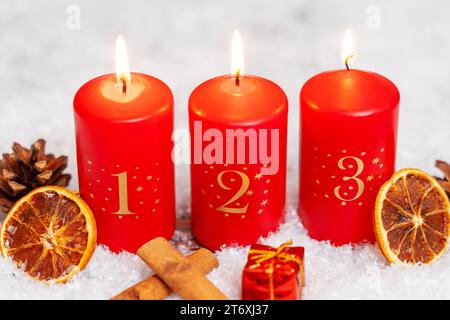 Bavaria, Germany - November 10, 2023: Three red candles burning for the 3rd Advent surrounded by winter decorations *** Drei rote Kerzen brennen zum 3. Advent umgeben von winterlicher Dekoration Stock Photo