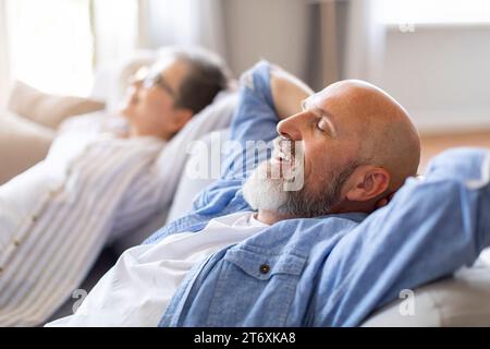 Happy Relaxed Senior Spouses Leaning Back On Comfortable Couch Stock Photo