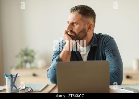 Depressed middle aged man sits troubled at laptop in office Stock Photo