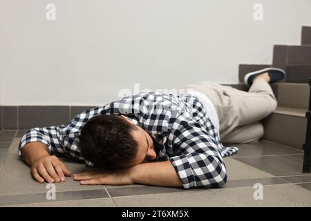 Unconscious man lying on floor after falling down stairs indoors Stock Photo