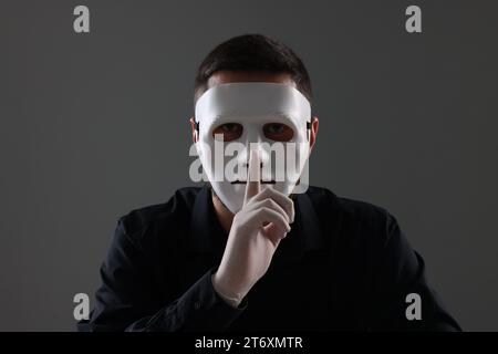 Man in mask and gloves showing hush gesture against grey background Stock Photo