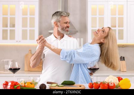Happy affectionate couple dancing while cooking together in kitchen Stock Photo