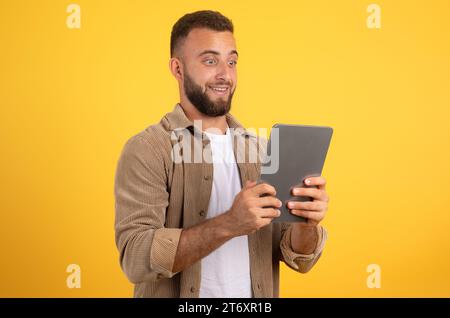 Shocked funny european millennial man with beard look at tablet, using app for social networks Stock Photo