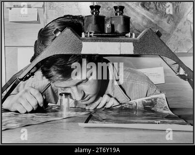 KOREAN WAR FIFTH AIR FORCE Aerial reconnaisance intelligence with a photograph of a Communist gun position in front of him, Sgt. James E. Kindseth looks carefully through his magnifier. 1950 South Korea Stock Photo