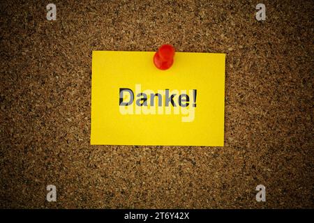 A yellow paper note with the word Danke! (Thank you in German) on it pinned to a cork board. Close up. Stock Photo