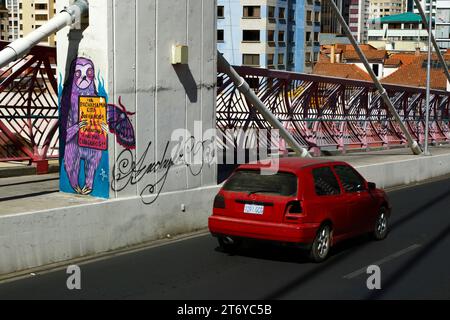 La Paz, Bolivia, 7th July 2022: A red car drives past a mural on a pillar of the Puente Gemelo / Twin Bridge of a sloth protesting against chaqueos / fires started deliberately to clear the tropical forests of he Chiquitania and Amazon regions of the Bolivian lowlands. Deforestation has become a huge problem in Bolivia in the last decade in particular; in 2022, Global Forest Watch placed Bolivia third in the world for primary forest loss. Much of the deforestation is government policy to expand the country's agricultural frontier to produce soya and cattle for export to especially China. Stock Photo