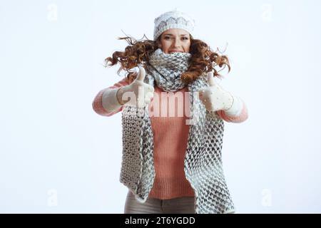 Hello winter. stylish woman in sweater, mittens, hat and scarf against white background showing thumbs up and jumping. Stock Photo