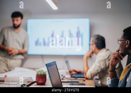 Diverse professionals discuss architectural blueprints and graph charts, collaborating in a modern conference room. Stock Photo