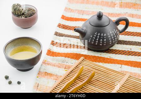 Chinese clay teapot with floral blooming tea ball tea cup against white backdrop Stock Photo