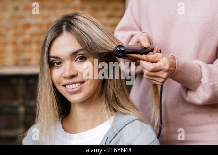 Smiley woman getting her hair straightened home Stock Photo