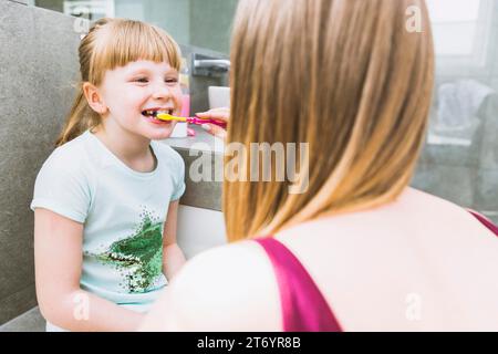 Faceless mother brushing teeth daughter Stock Photo