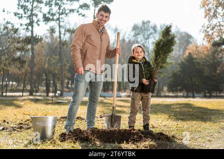 Man using shovel dig hole planting tree while posing son Stock Photo