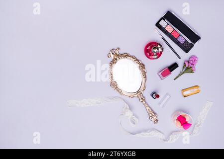 Vintage hand mirror lipstick nail varnish sponge perfume bottle eyeshadow palette purple background Stock Photo