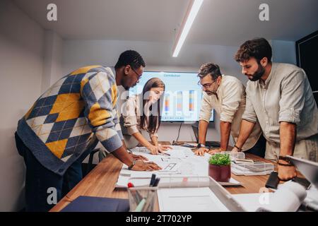 Multinational team of architects, engineers and business team collaborating in board room. Discussing blueprint, brainstorming, sharing ideas. Stock Photo
