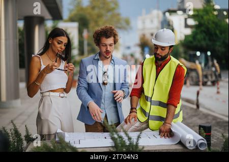 Diverse architects and engineers collaborating on a construction project, discussing blueprints and developing innovative ideas outdoors. Stock Photo