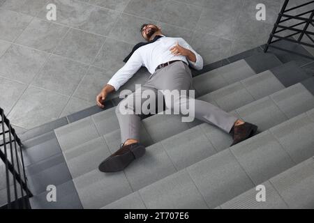Unconscious man lying on floor after falling down stairs indoors Stock Photo