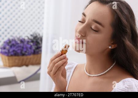 Beautiful young woman with bottle of essential oil indoors Stock Photo