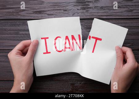 Motivation concept. Woman making phrase I Can from I Can't by tearing paper at wooden table, top view Stock Photo