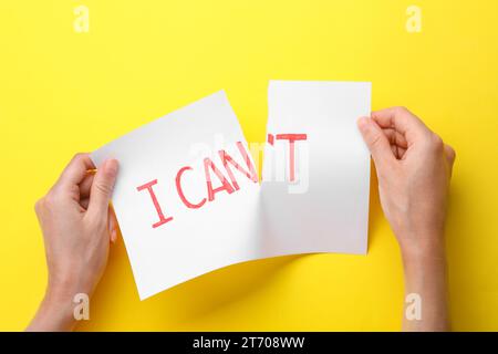 Motivation concept. Woman making phrase I Can from I Can't by tearing paper on yellow background, top view Stock Photo