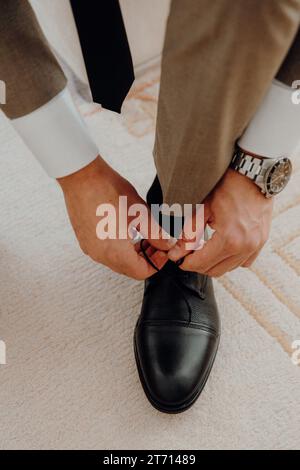 A man in a formal suit is in the process of tying his shoes, getting ready for a wedding ceremony Stock Photo