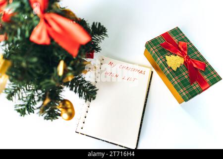 open notepad with christmas wish list text. decorated christmas tree and gift box on background. Stock Photo