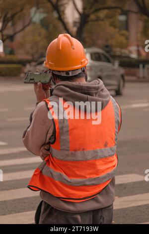 A construction worker in a safety helmet standing on a city street while using his phone. Stock Photo