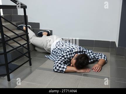 Unconscious man lying on floor after falling down stairs indoors Stock Photo