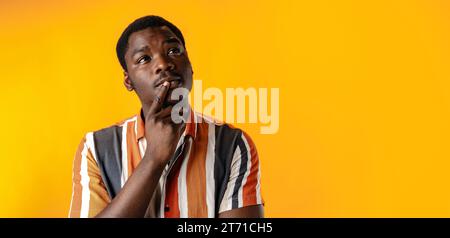 Young african man thinking against yellow background Stock Photo