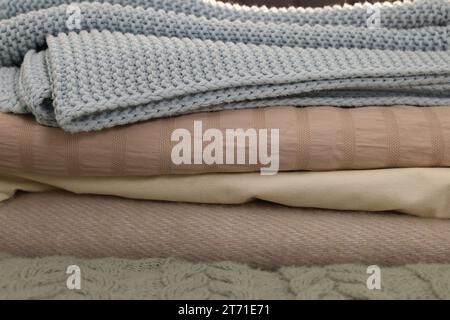 Stack of different folded blankets on bed, closeup. Home textile Stock Photo