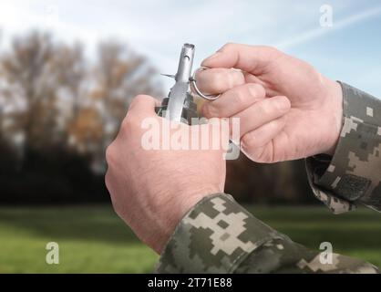 Soldier pulling safety pin out of hand grenade outdoors, closeup Stock Photo