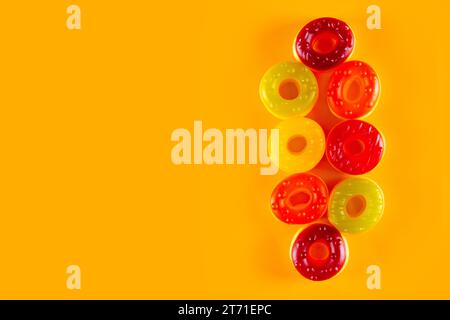 Few jelly candies in the shape of donut lie on light orange background. Bold surface for sweet circular confections Stock Photo