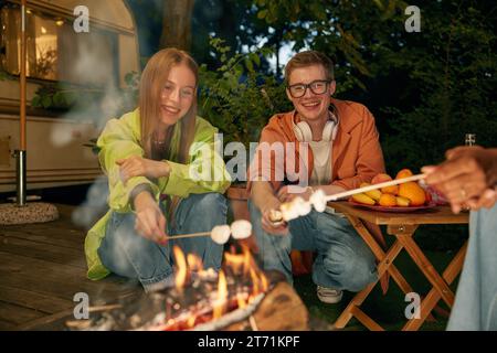 Friends roasting marshmallows over bonfire at van motor home Stock Photo