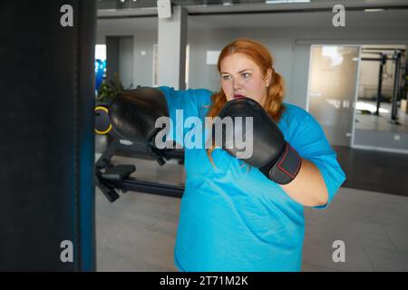 Concentrated fat woman using boxing gloves doing punching exercises Stock Photo